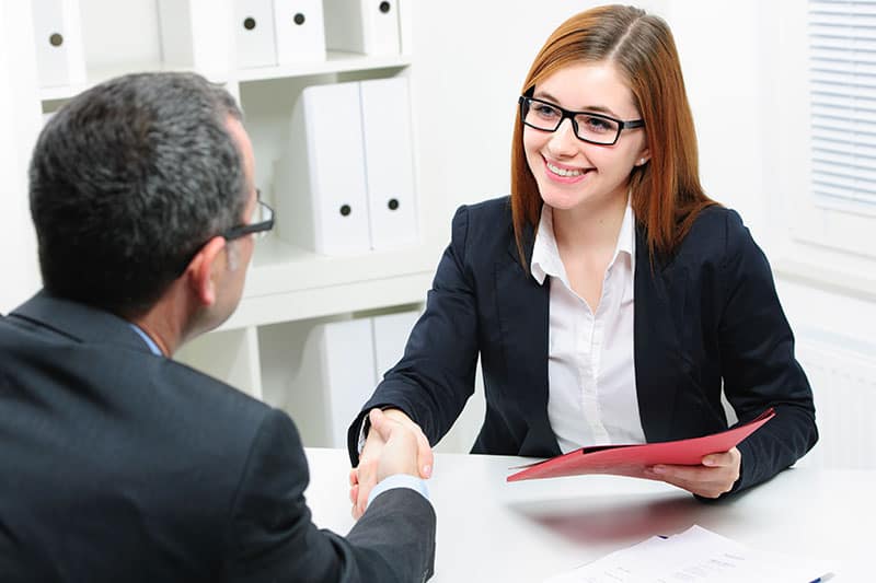 employer-shaking-hands woman shaking hands with male sitting at desk